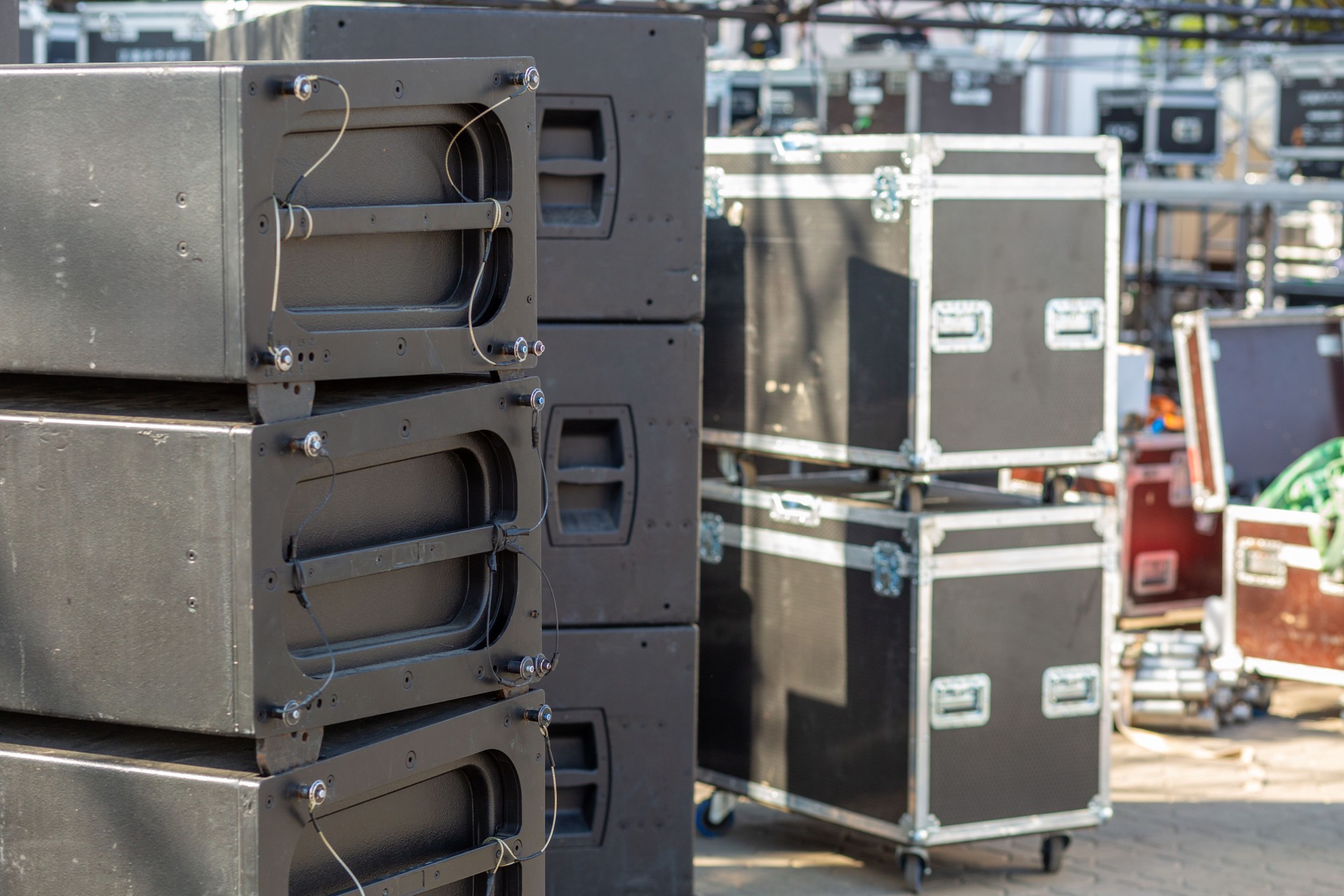 Stacks of sound equipment and lighting gear are arranged at an outdoor venue, ready for a concert.